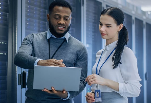 IT lady and guy looking at laptop in server room