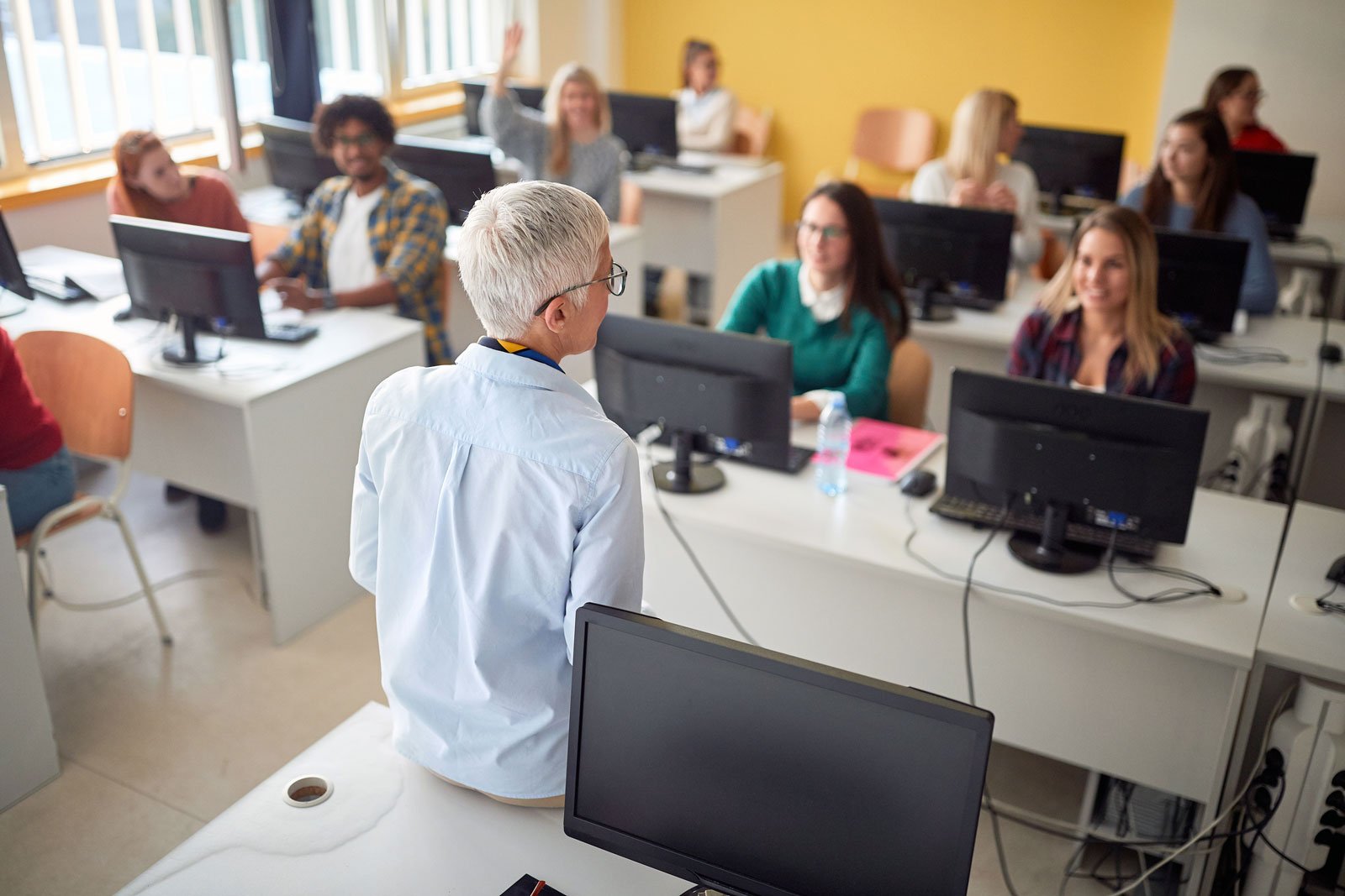 Teacher in front of room of people learning with computers