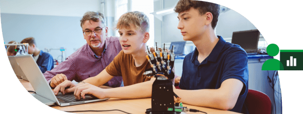 Teacher helping two students with a robotic hand model at a computer in a classroom setting.