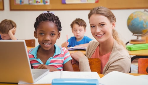 Cute pupil using computer with teacher at the elementary school