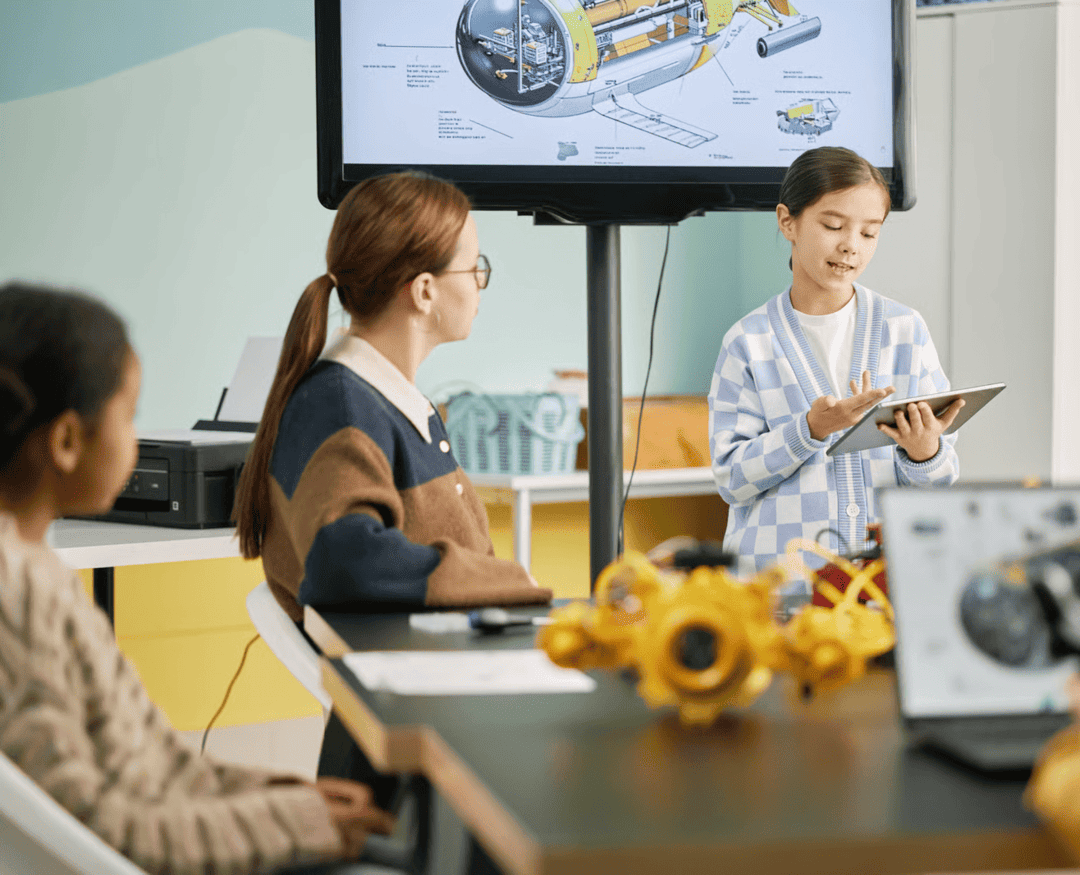 Student presenting in a classroom using tech devices, with teacher and peers engaged: an example of how technology planning for schools can support learning