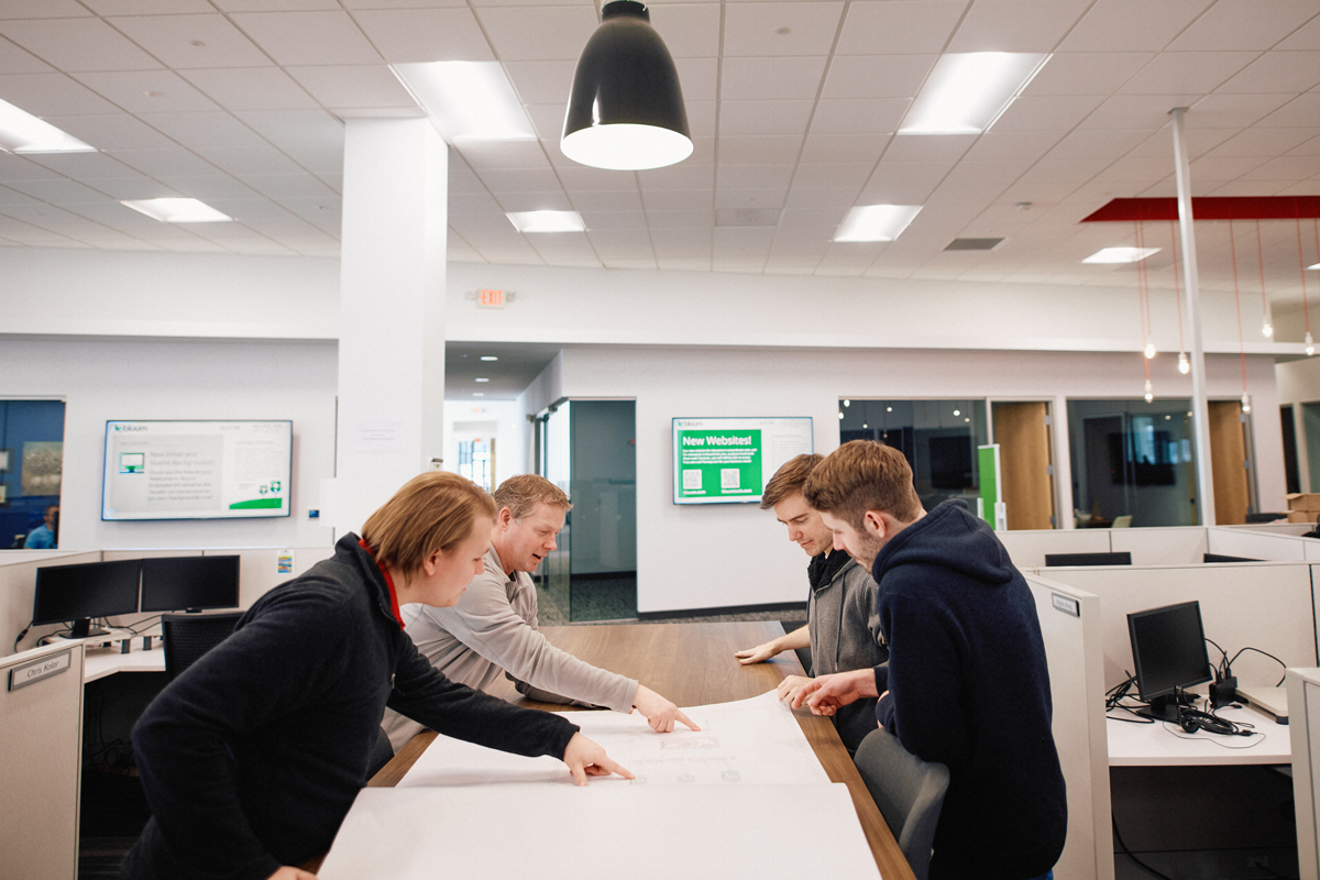 4 guys pointing at a plans on a table