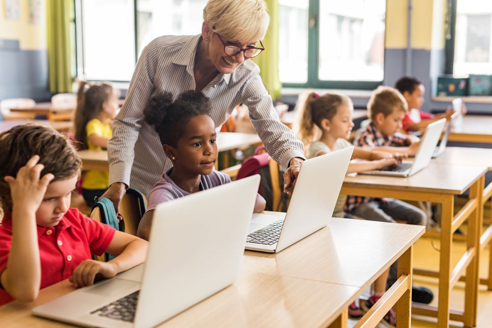 Teacher assisting school kids using their laptops